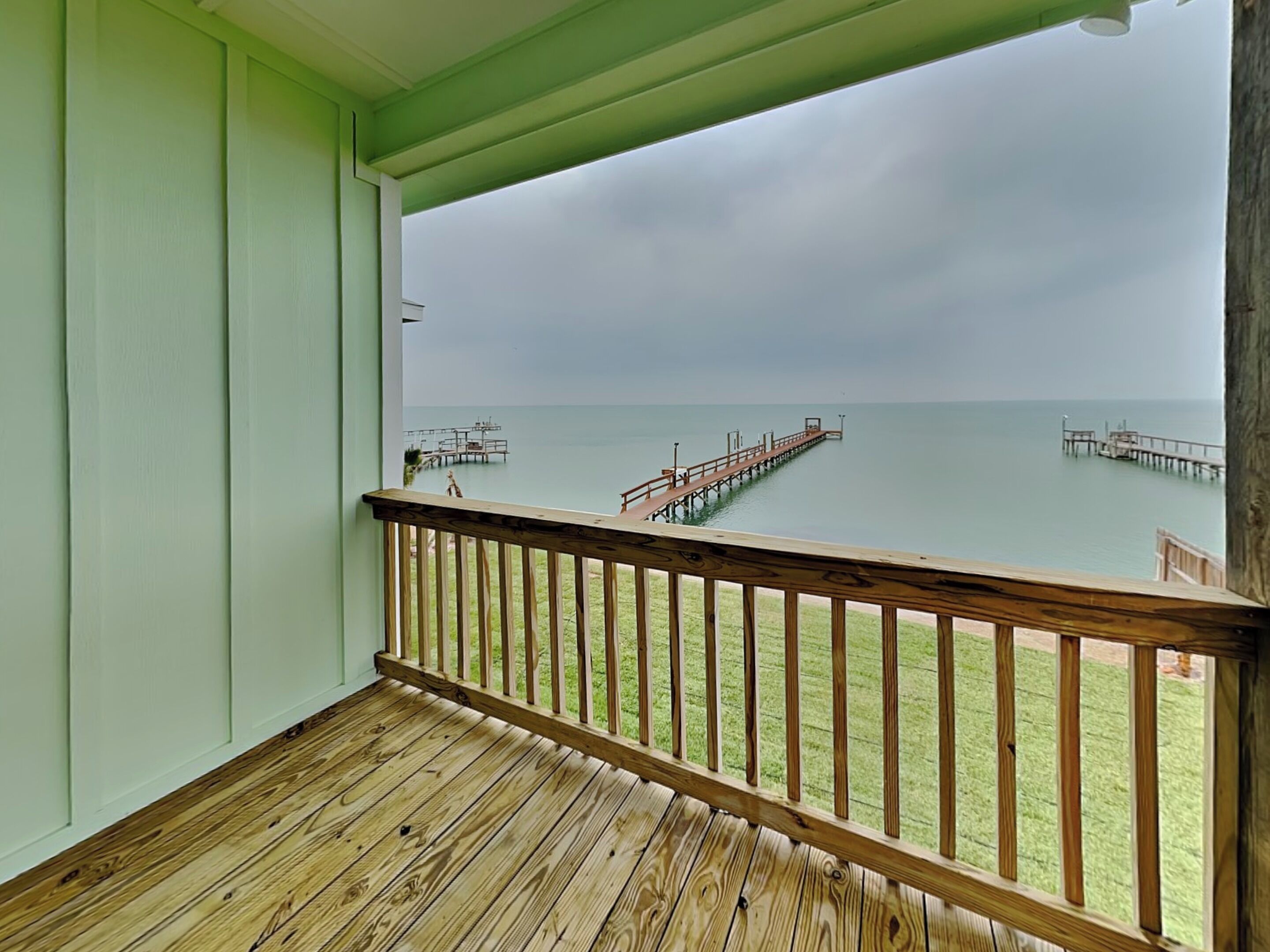A wooden deck with a railing, a view of the ocean, and a pier extending into the water.