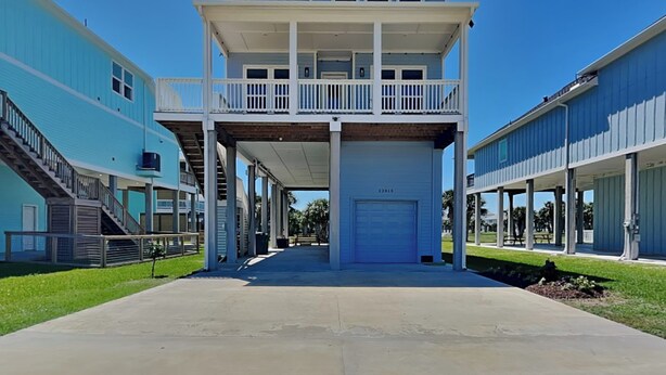 A two-story building with a balcony, a garage, and a covered walkway. - Buckin Beach House (Galveston)