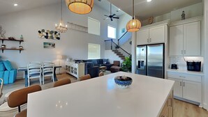 A modern kitchen with a large island, white cabinetry, and a stainless steel refrigerator. - Buckin Beach House (Galveston)