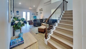 A spacious living area with a staircase, wooden flooring, and a dining table with books. - Buckin Beach House (Galveston)