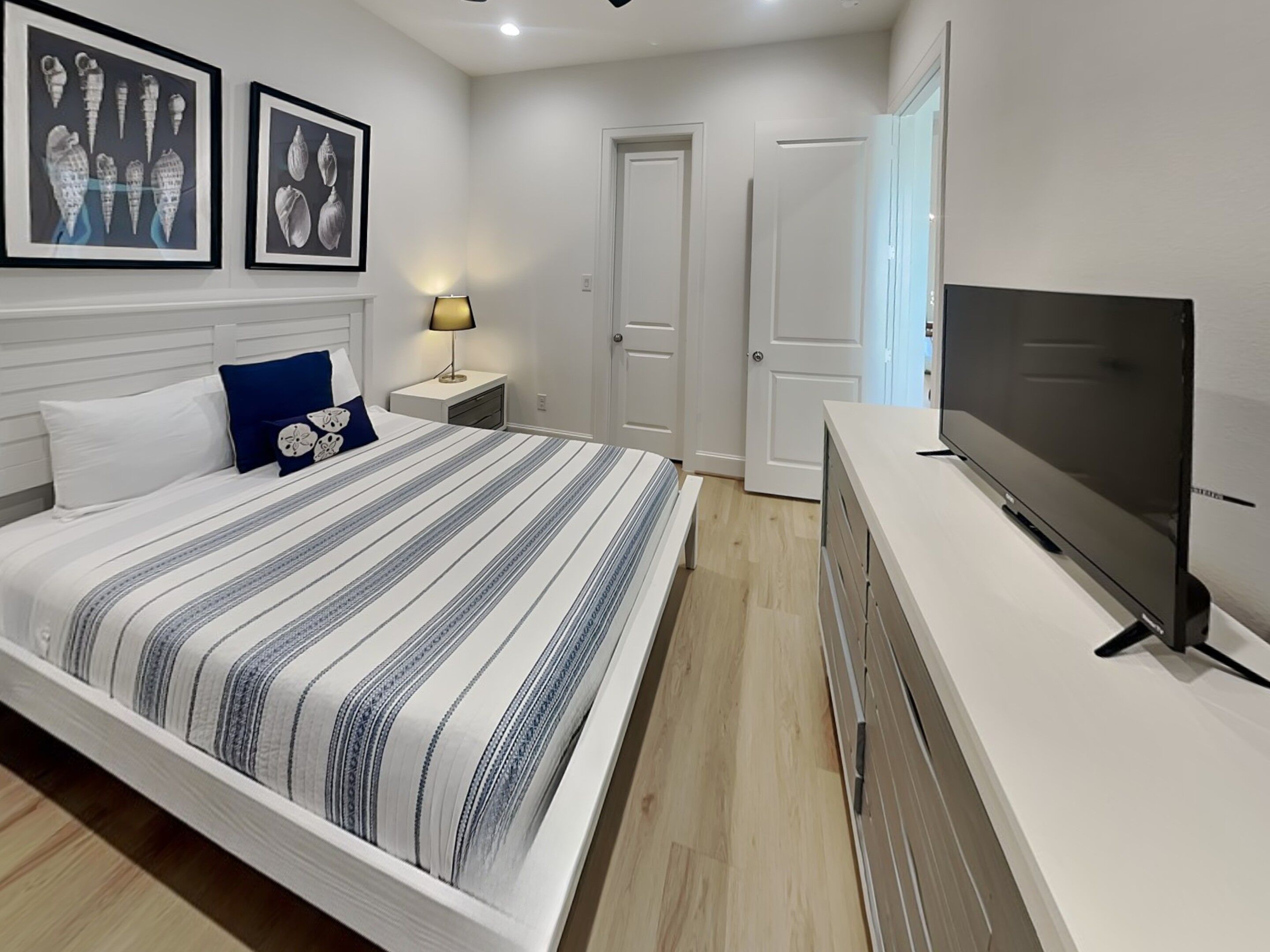 Een slaapkamer met een bed, een televisie, een nachtkastje en lijstjes met foto’s aan de muur.