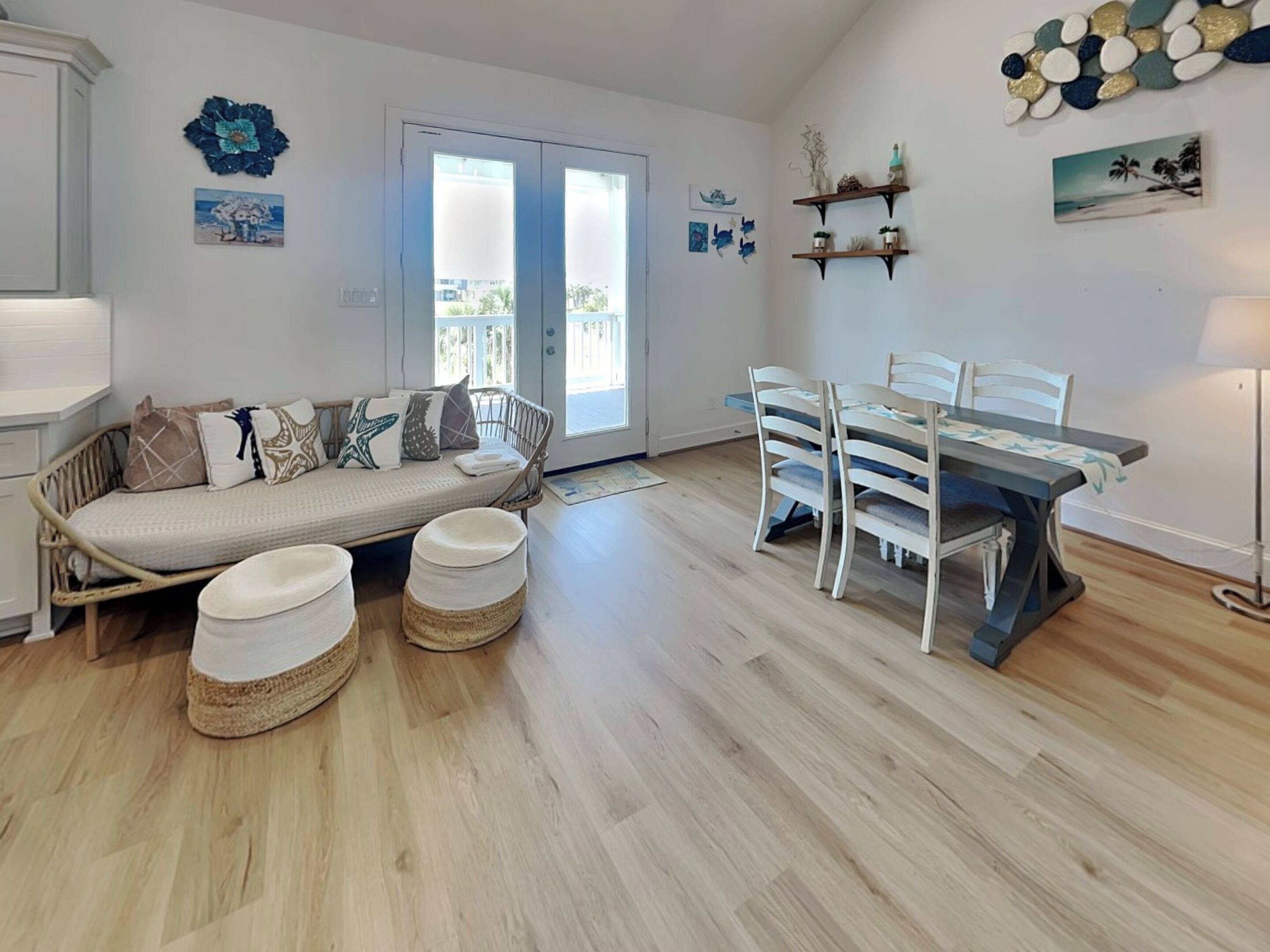 A room with a sofa, ottomans, a dining table with chairs, a lamp, and wall decorations.