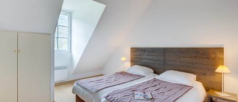 A bedroom with two beds, a wooden headboard, bedside lamps, a magazine on the bed, and a skylight.