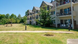 Un edificio residencial de varios pisos con balcones, una mesa de picnic y un patio cubierto de césped.
