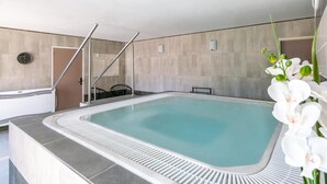 Una piscina interior moderna con superficie de agua azul cristalina, un reloj en la pared y una silla cerca de la piscina.