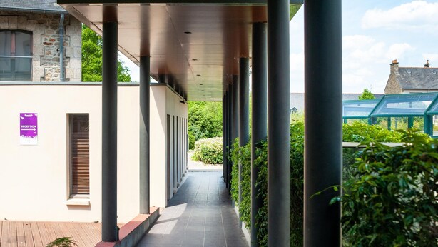 A covered walkway with columns, a reception sign, and a view of greenery and buildings. - Cozy 2-person Studio in Correze (Dinan)