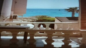 Een balkon met uitzicht op zee, een palmboom en een gebouw op de achtergrond.