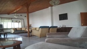 Een ruime woonkamer met een hoge plafond, een zithoek, een glazen salontafel en een kroonluchter.