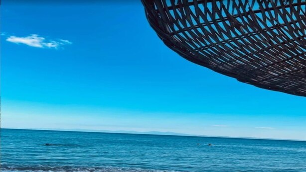 Een strand met een heldere lucht, een rustige zee en een grote, donkere, bolvormige structuur.