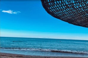 Una playa con cielo despejado, mar tranquilo y una estructura esférica grande y oscura.