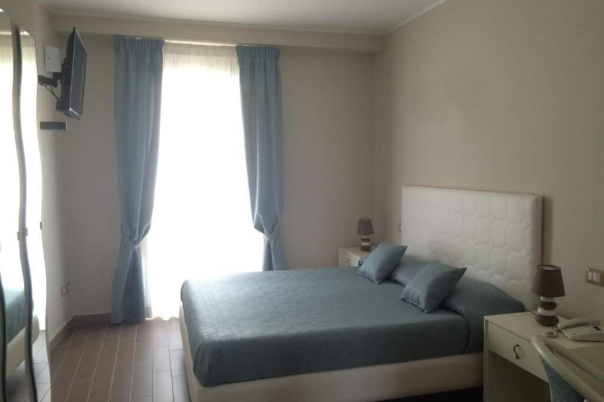 Une chambre à coucher avec un lit, des rideaux, une table de chevet et une lampe.