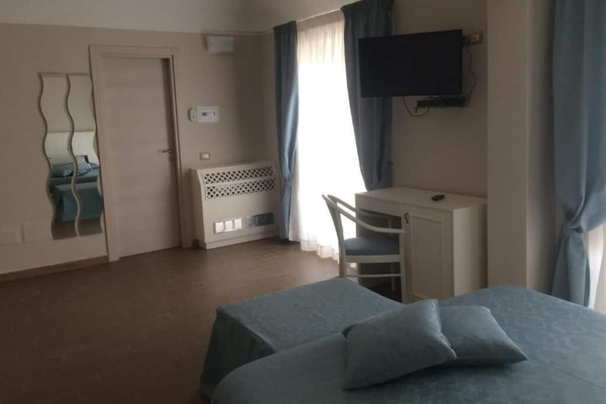 Une chambre d’hôtel avec un lit, un bureau, une chaise, une télévision, une porte et une fenêtre avec des rideaux.