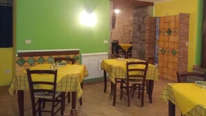 A dining area with tables covered in yellow tablecloths, wooden chairs, and a stone wall with a tiled pattern. - hotel santt'anna (Floresta)