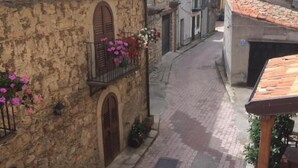 A narrow cobblestone street flanked by stone buildings with arched doorways and balconies adorned with flowers. - hotel santt'anna (Floresta)