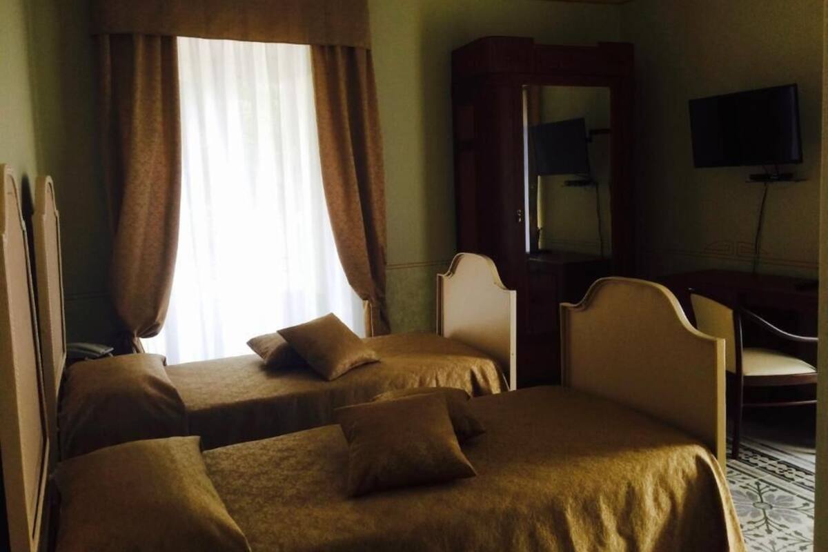 Une chambre d’hôtel avec deux lits, un bureau, une chaise, une télévision et une grande fenêtre avec des rideaux.