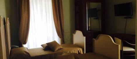 A hotel room with two beds, a desk, a chair, a television, and a large window with curtains.