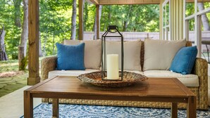 Une véranda abritée avec un canapé en osier, une table en bois et une bougie dans une lanterne.