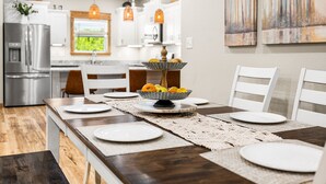 Une cuisine moderne avec des meubles blancs, des appareils en acier inoxydable et un coin repas doté d’une table en bois, mise pour quatre personnes.