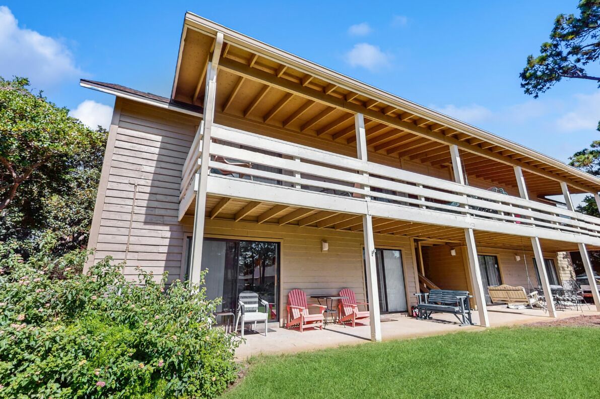 A two-story building with a covered patio area, large windows, and a grassy lawn.
