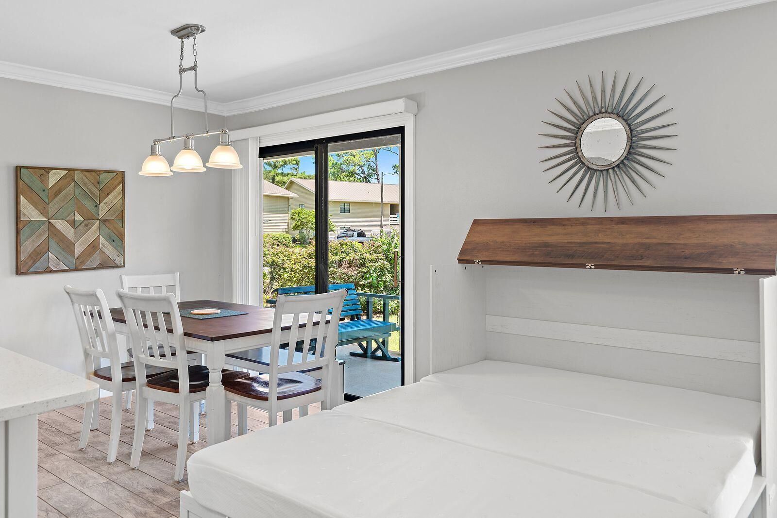 Uma área de refeições com uma mesa e cadeiras, um lustre pendurado e vista para o exterior através de uma porta de vidro.