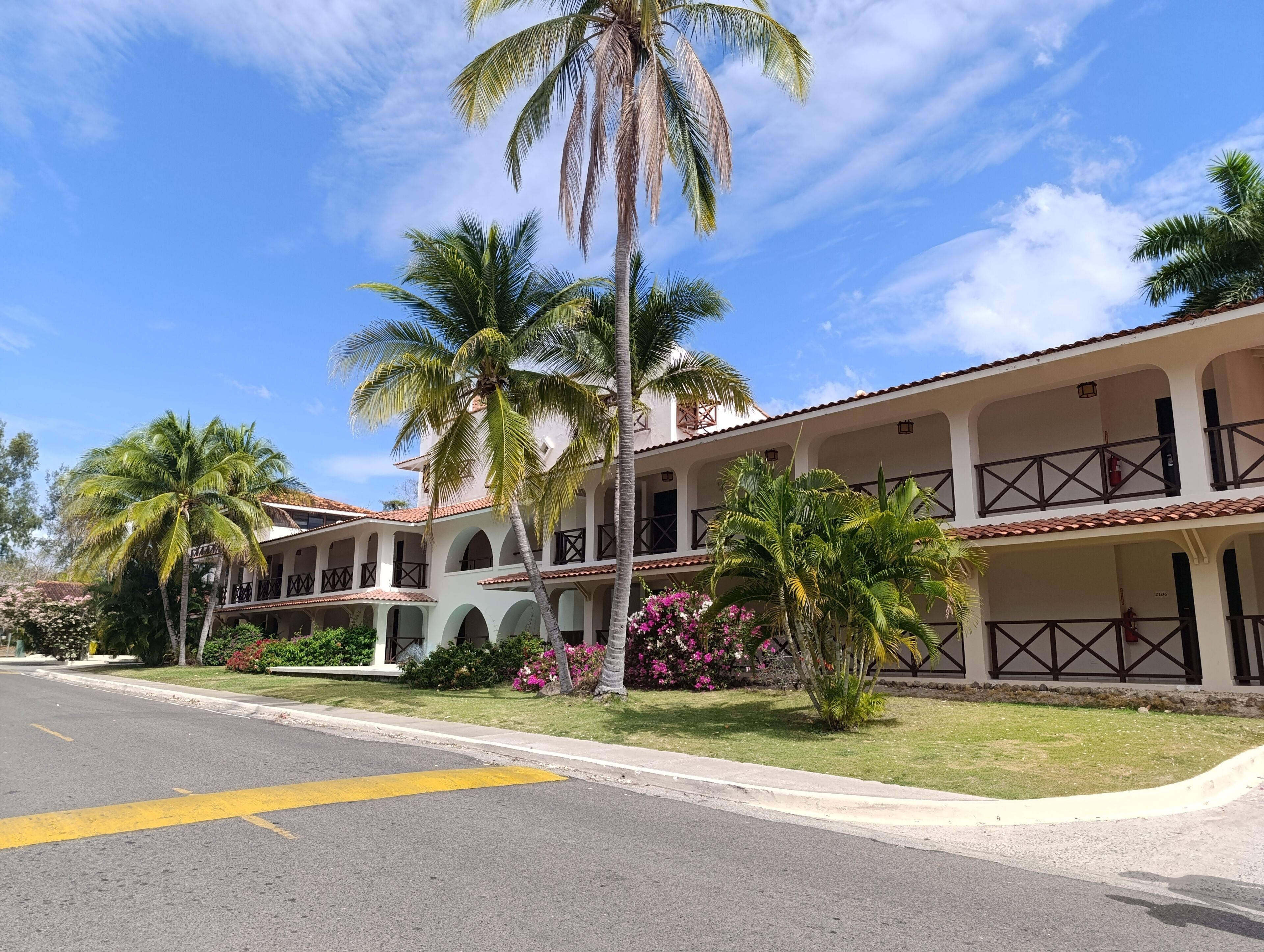 A two-story hotel with a courtyard, palm trees, and a clear sky.