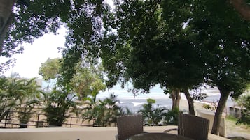 An outdoor seating area with wicker furniture, surrounded by trees and a view of the sea.