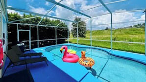 A covered outdoor swimming pool with lounge chairs, inflatable toys, and a view of the surrounding landscape.