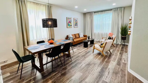 A modern living room with a dining area, wooden flooring, and a ceiling fan.