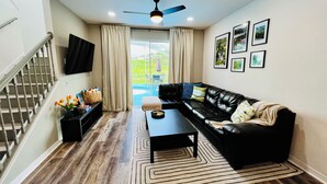 A living room with a black leather sofa, a coffee table, a TV mounted on the wall, and a staircase.