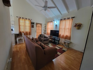 Ein Wohnzimmer mit einer Couch, Fernseher, Deckenventilator und Holzboden.