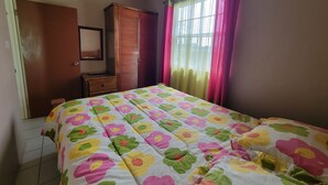 A bedroom with a bed, a wardrobe, a mirror, and a window with curtains.