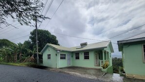 A two-story building with a green facade, a covered porch, and a small garden area.