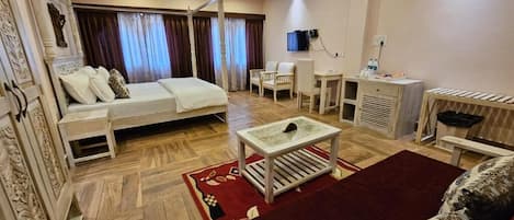 A hotel room with a bed, a desk, a chair, a radiator, and a television.