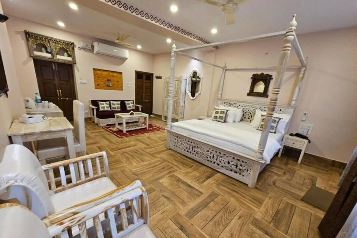 Una cama con dosel, un sofá, una mesita y un espejo en una habitación luminosa con suelo de madera.