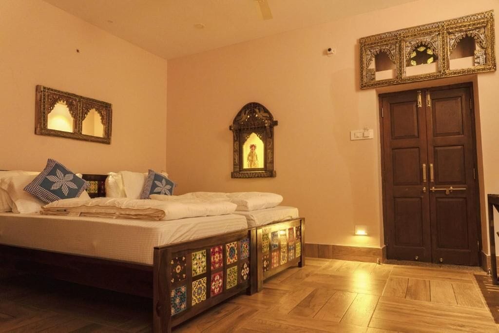A bedroom with a bed, a wooden floor, a wall-mounted mirror, and a door.