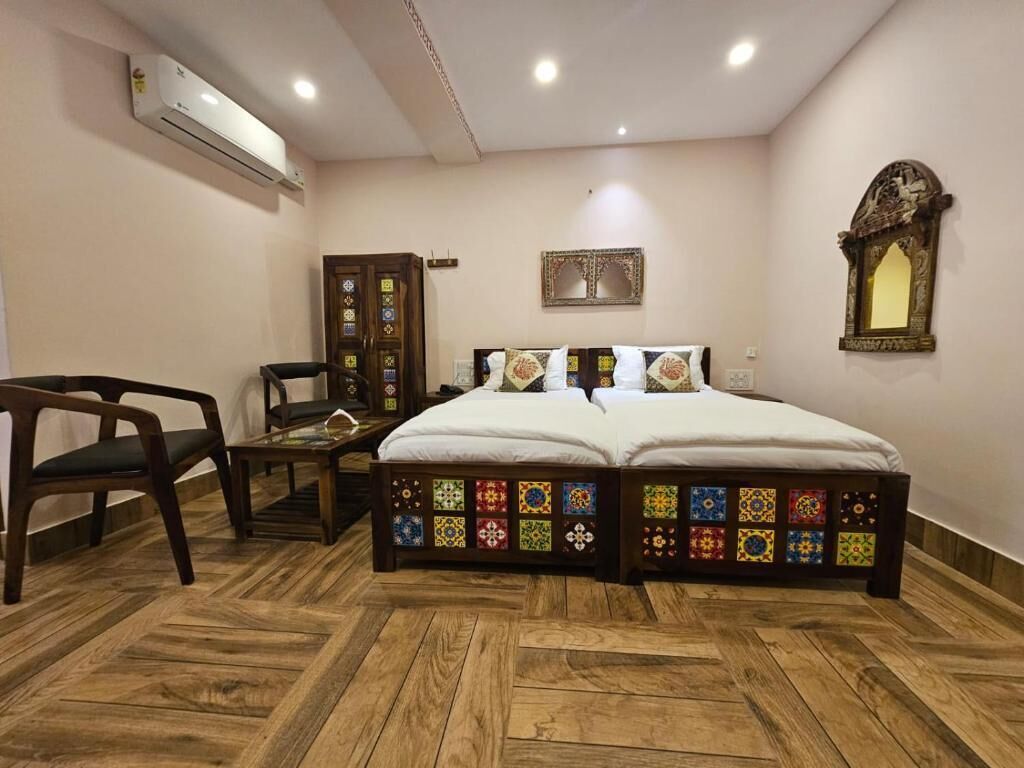 A bedroom with a wooden floor, a bed with colorful panels, a desk with a chair, and an air conditioning unit.