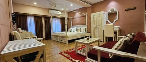 A bedroom with a four-poster bed, a sitting area with a sofa and armchairs, a small table, and a wardrobe.