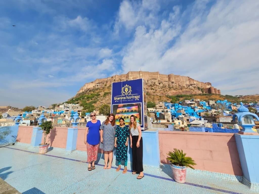 A group of people standing in front of a sign with a fort in the background.