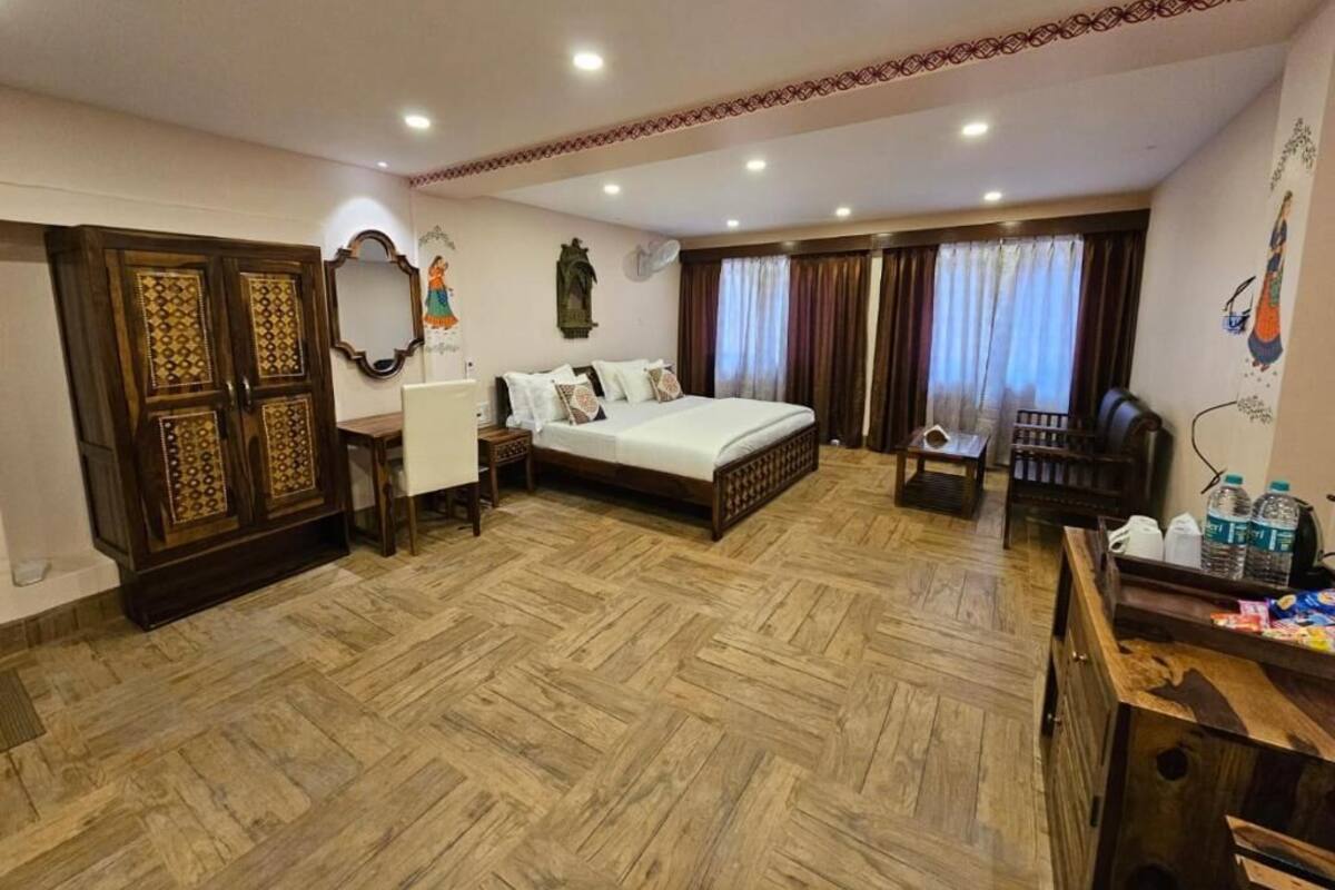 Habitación de hotel con piso de madera, cama, escritorio, silla, armario y ventana con cortinas.