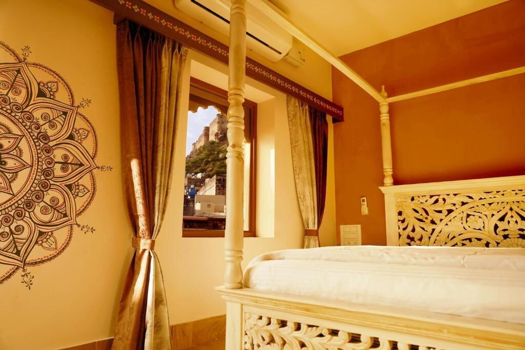 A room with a four-poster bed, a decorative wall with a mandala, and a view through a window.