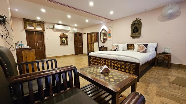 Une chambre d’hôtel avec un lit, un banc en bois, une table et un miroir.