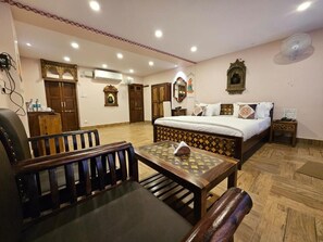 A hotel room with a bed, a wooden bench, a table, and a mirror. - Khamma Heritage (Jodhpur)