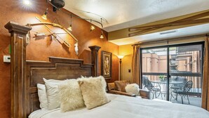 Ein Hotelzimmer mit einem großen Bett, einem hölzernen Kopfteil, einem Balkon mit Sitzmöbeln und Blick auf die Stadt.