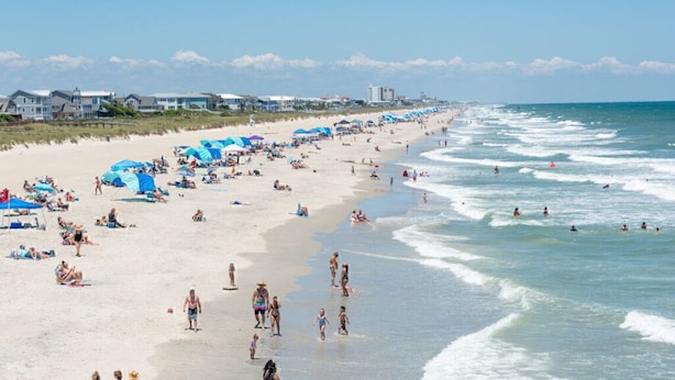 A beach with people sunbathing and swimming, and buildings in the background. - Harriss-James Carriage House Unit B, 0.3 Mi from Historic Downtown (Wilmington)