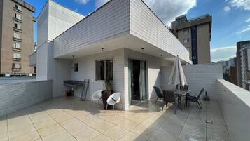A modern building with a tiled exterior, a balcony with chairs and a table, and a view of surrounding buildings.