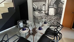 A dining area with a glass table, black chairs, and a mural of a street scene. - LK Santo Antônio 4 (Belo Horizonte)