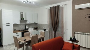 Une cuisine moderne avec des meubles blancs, une table à manger avec des chaises, un canapé rouge et un luminaire au plafond.
