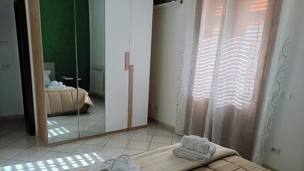 Une chambre à coucher avec un lit, un miroir, une armoire et une fenêtre avec des rideaux.