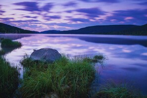 A calm lake with a rock in the foreground, surrounded by grass and hills in the background. - Forestum - Black Forest Luxury Apartments - Apartment Fuchs with sauna (Sankt Blasien)