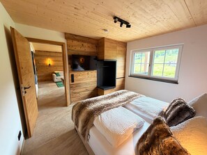 Ein Schlafzimmer mit einem Bett, einem Fernseher, einem Fenster und einer Holzbalkendecke.